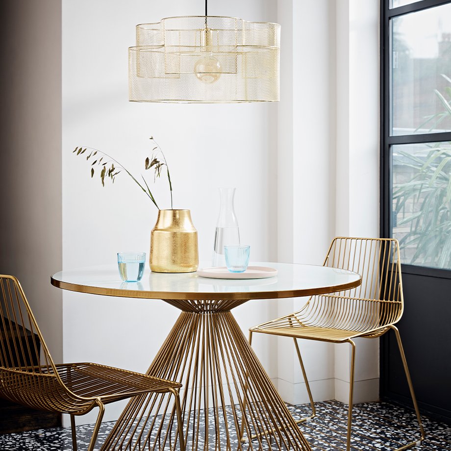 A glass-topped gold table with matching gold wire-backed chairs.